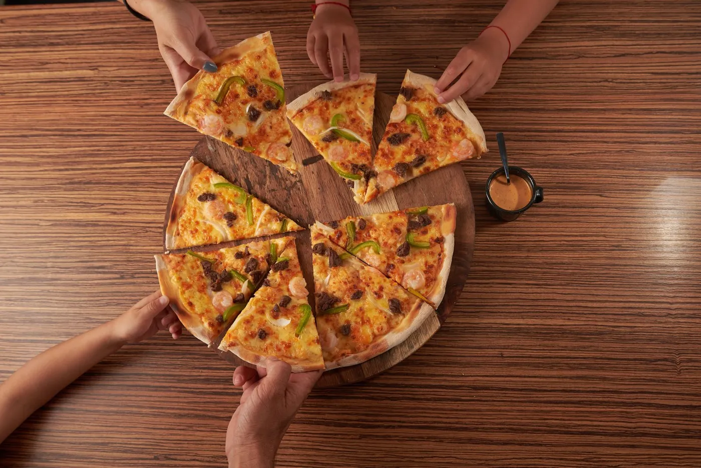 Mãos pegando fatias de uma pizza numa mesa de madeira